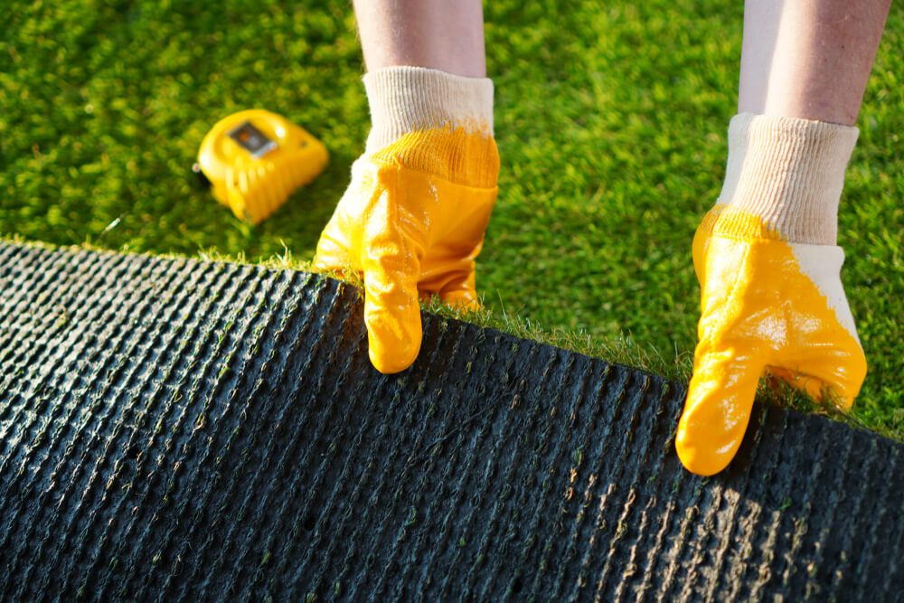 Worker Holds a Roll of Green Artificial Turf
