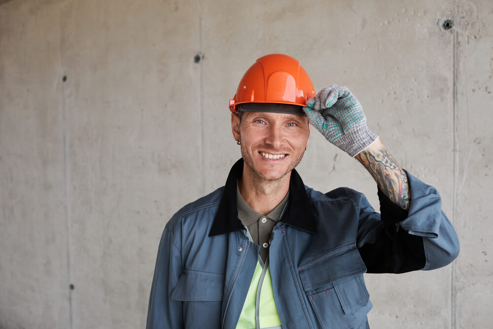 Portrait of Smiling Construction Worker Wearing Hardhat While Posing Against Concrete Wall