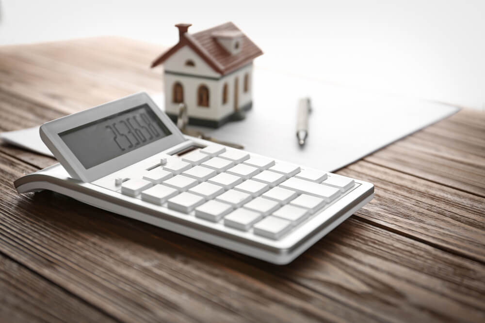 Calculator, House Model, Pen and Documents on Wooden Table.