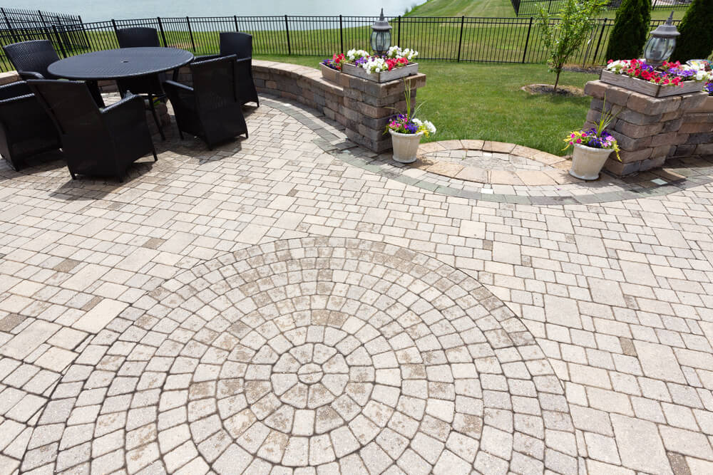 Ornamental Brick Paved Outdoor Patio With a Circular Design in the Bricks With Dining Furniture and Colorful Flowers