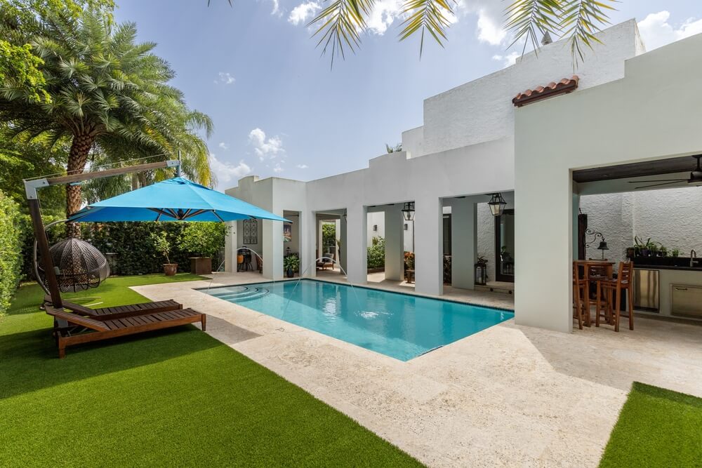 Backyard Of A Luxurious House With A Swimming Pool Artificial Grass Grill Zone And Some Tanning Chairs With An Umbrella