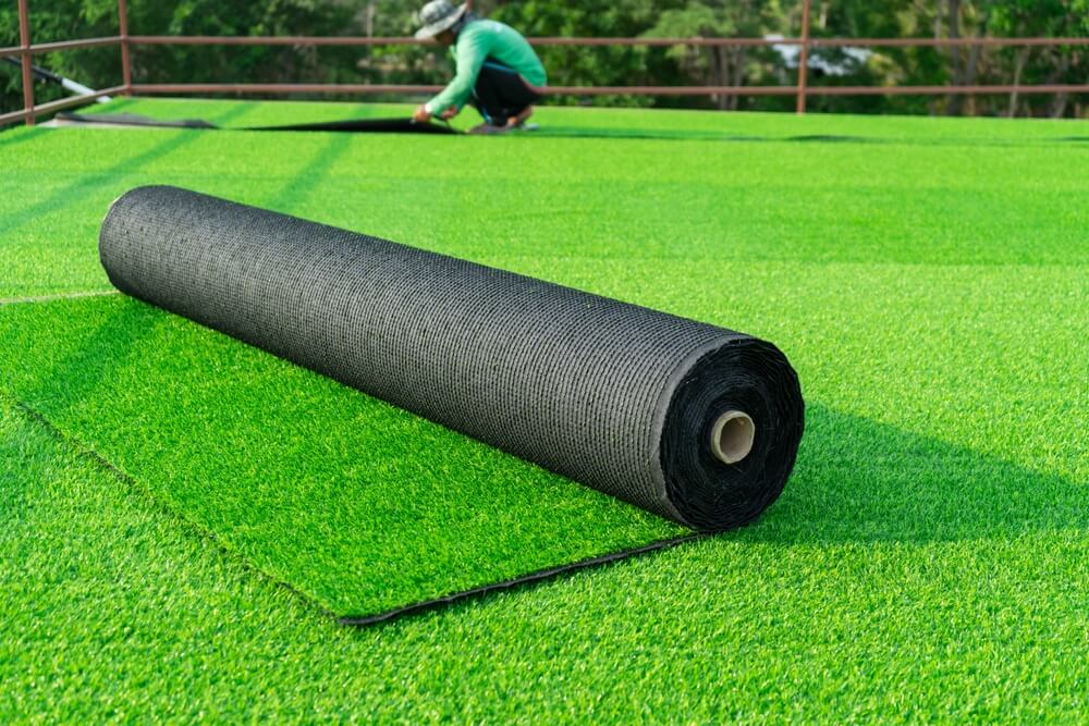 Roll Of An Artificial Turf Laying Background A Synthenic Grass Layer Greenering Of The Yard Of Green Lawn Background With Workers Pave The Counterfeit Grass