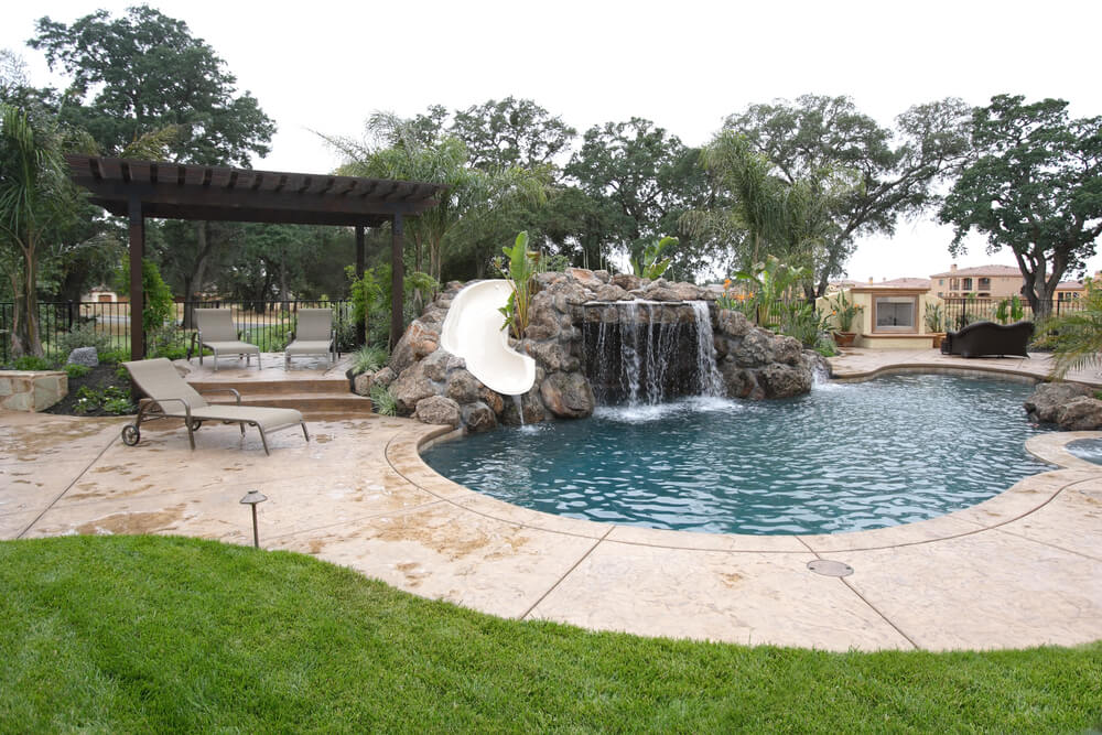 A waterfall in to a pool in a luxury backyard with tropical landscaping.