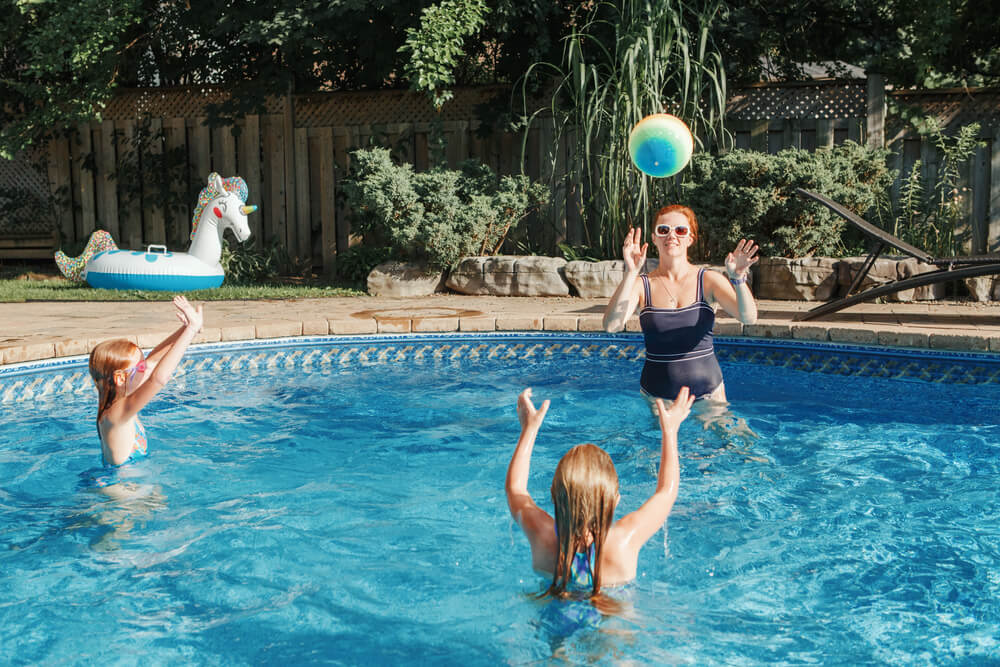 Mother playing volleyball with her daughters in a swimming pool in their backyard.