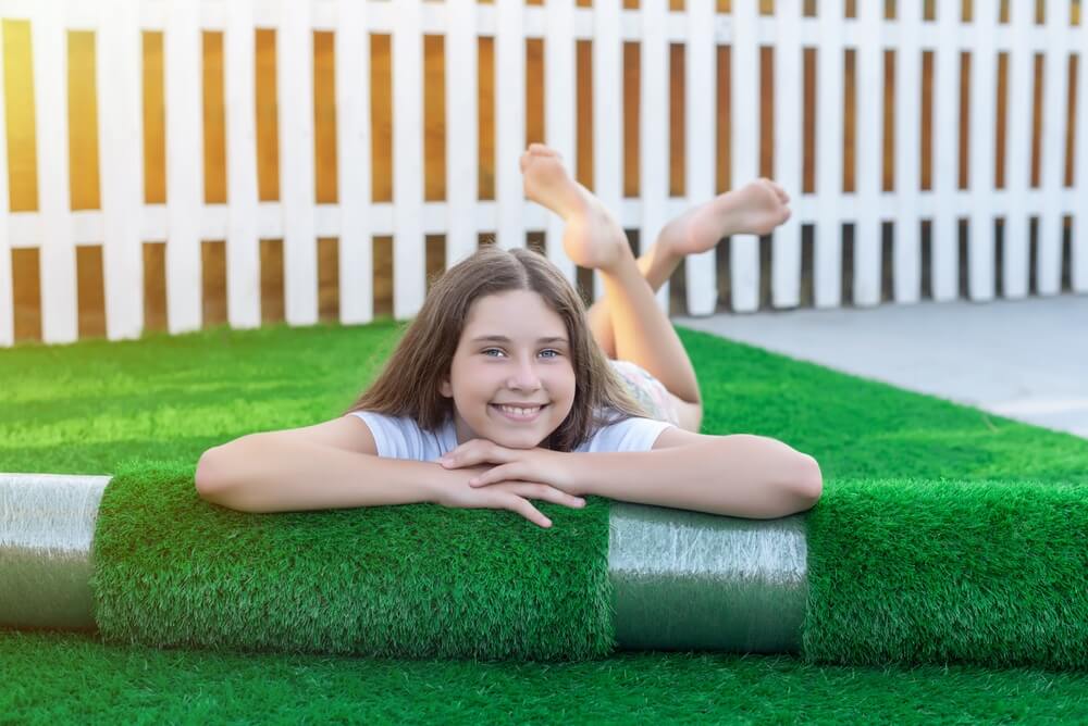 Smiling young girl lying on her terrace on a new roll of artificial turf.