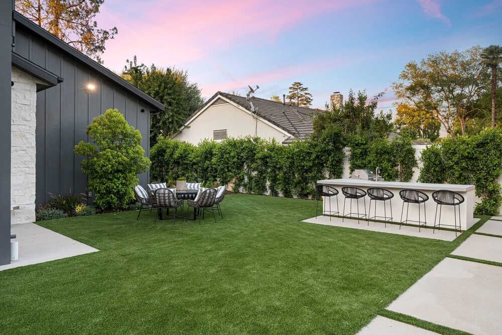 Modern backyard with artificial grass, outdoor dining set, and bar area.